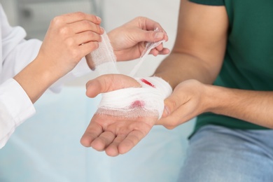 Female doctor applying bandage on young man's hand in clinic, closeup. First aid