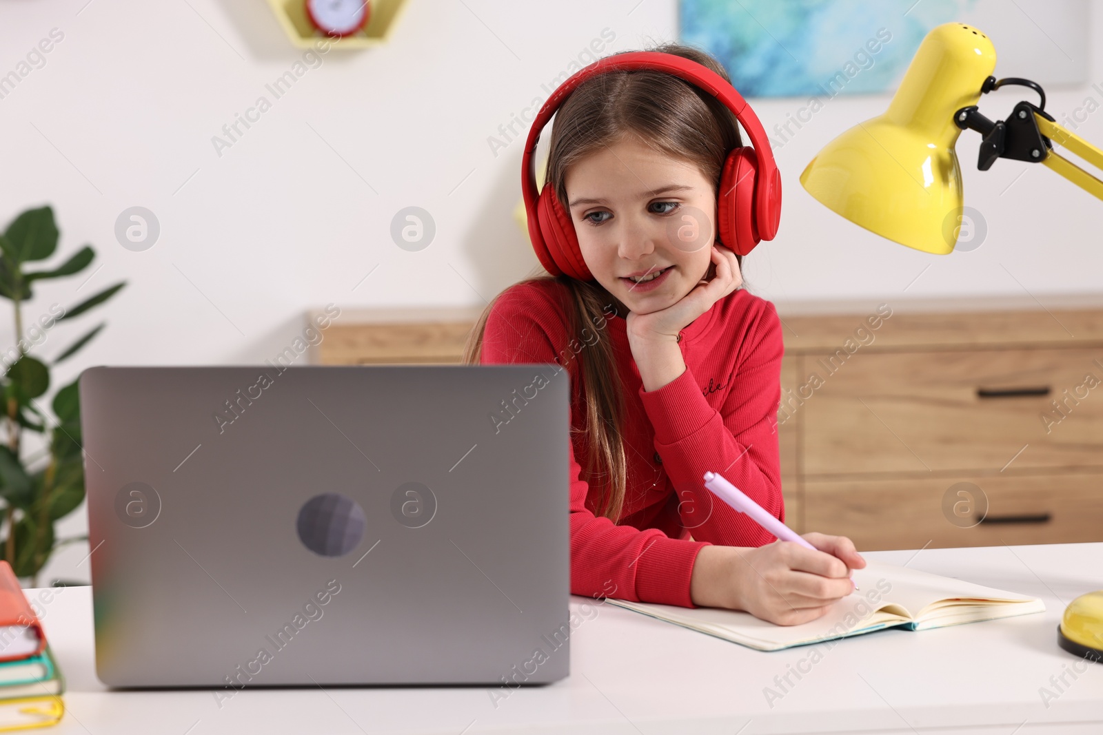 Photo of E-learning. Cute girl taking notes during online lesson at table indoors