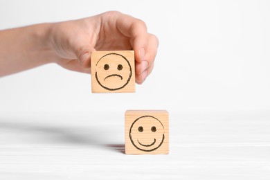 Image of Complaint. Woman choosing wooden cube with drawn sad face instead of another one with happy on white background, closeup