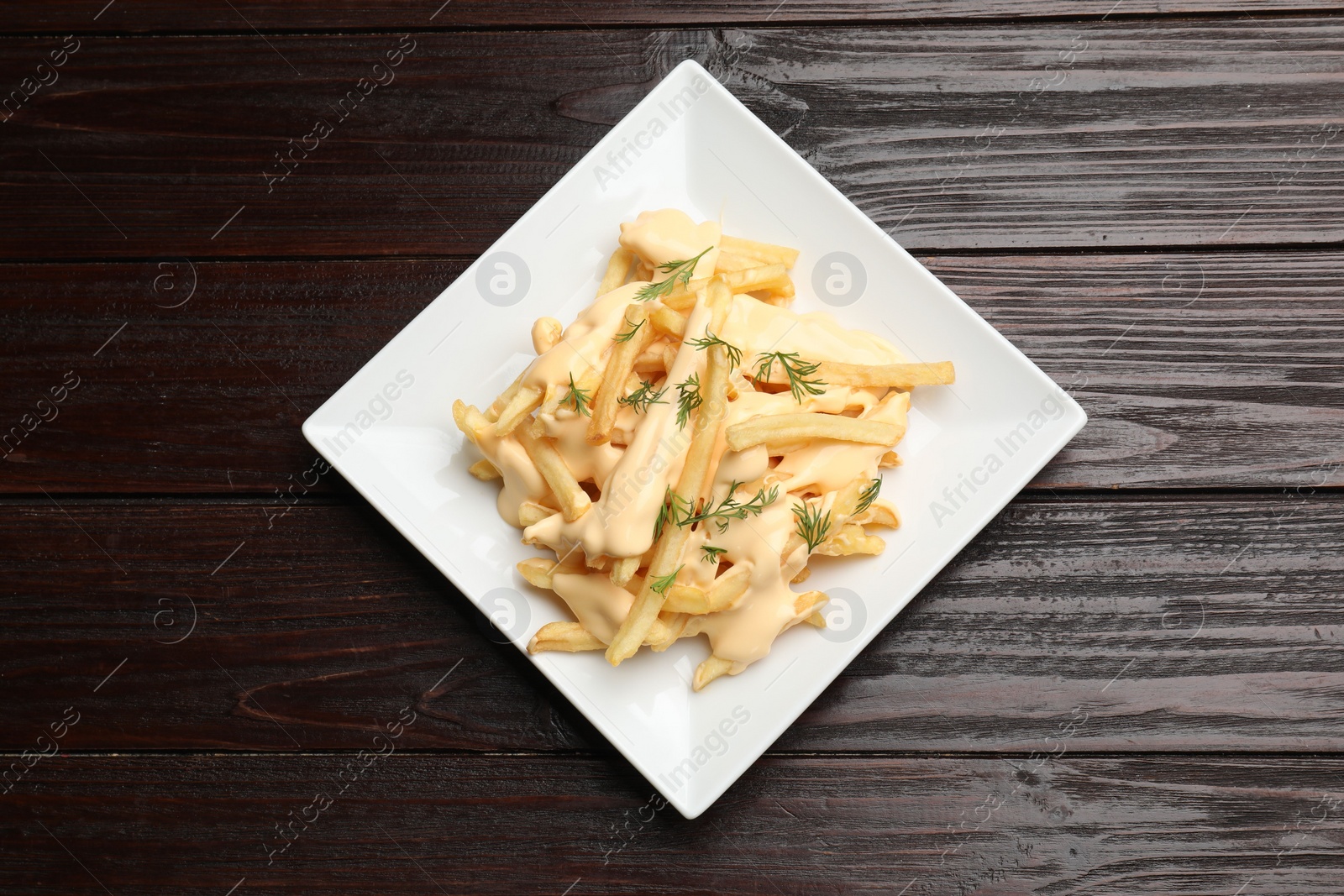 Photo of Delicious french fries with cheese sauce and dill on wooden table, top view