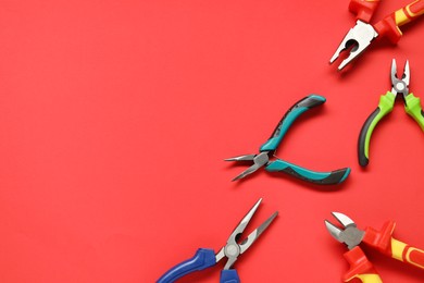 Photo of Different pliers on red background, flat lay. Space for text
