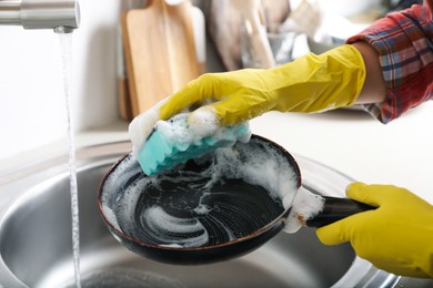 Photo of Woman washing dirty frying pan in sink indoors, closeup