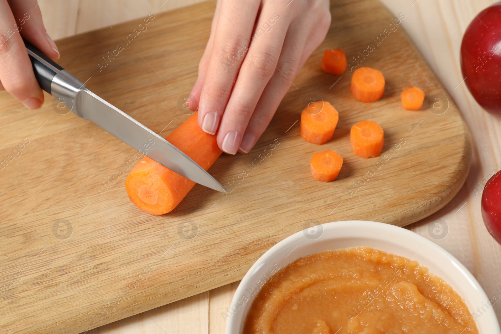 Photo of Woman cutting boiled carrot at wooden table. Preparing baby food