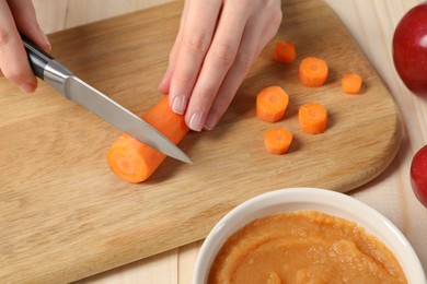 Photo of Woman cutting boiled carrot at wooden table. Preparing baby food