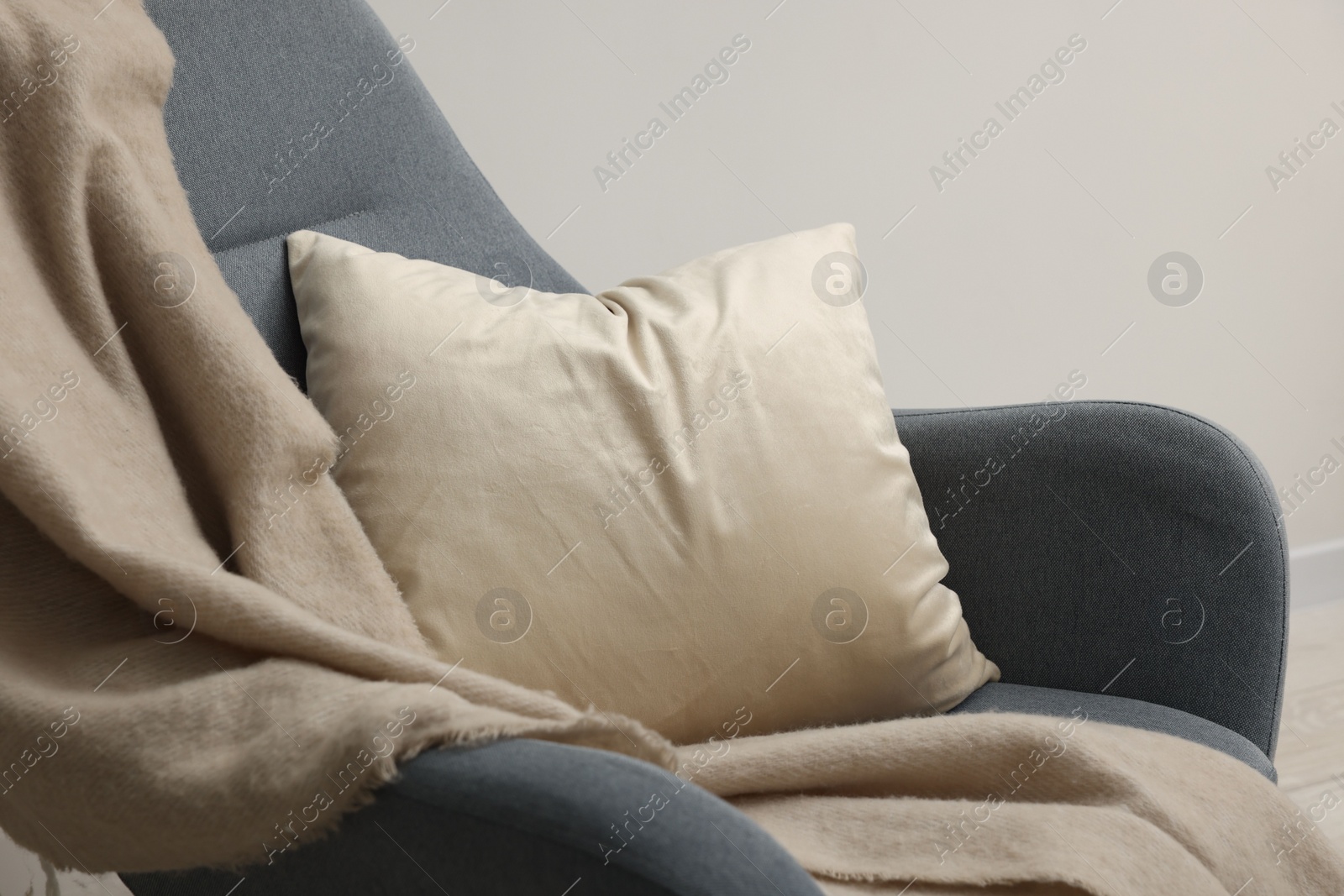 Photo of Soft pillow and blanket on armchair near light grey wall