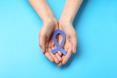 Photo of Woman holding blue awareness ribbon on color background, top view. Symbol of social and medical issues