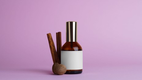 Bottle of luxurious perfume and spices on light purple background
