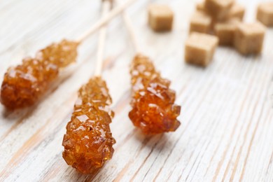 Photo of Sticks with sugar crystals on white wooden table, closeup. Tasty rock candies