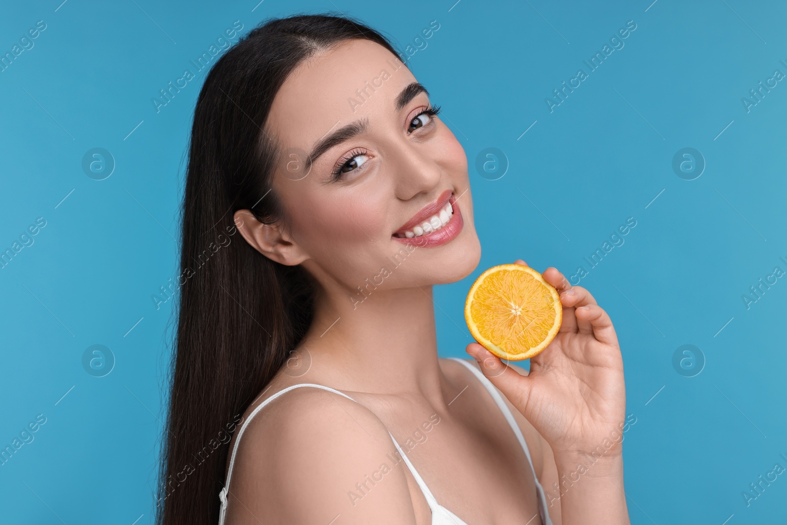 Photo of Beautiful young woman with piece of orange on light blue background