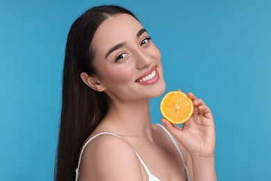 Photo of Beautiful young woman with piece of orange on light blue background