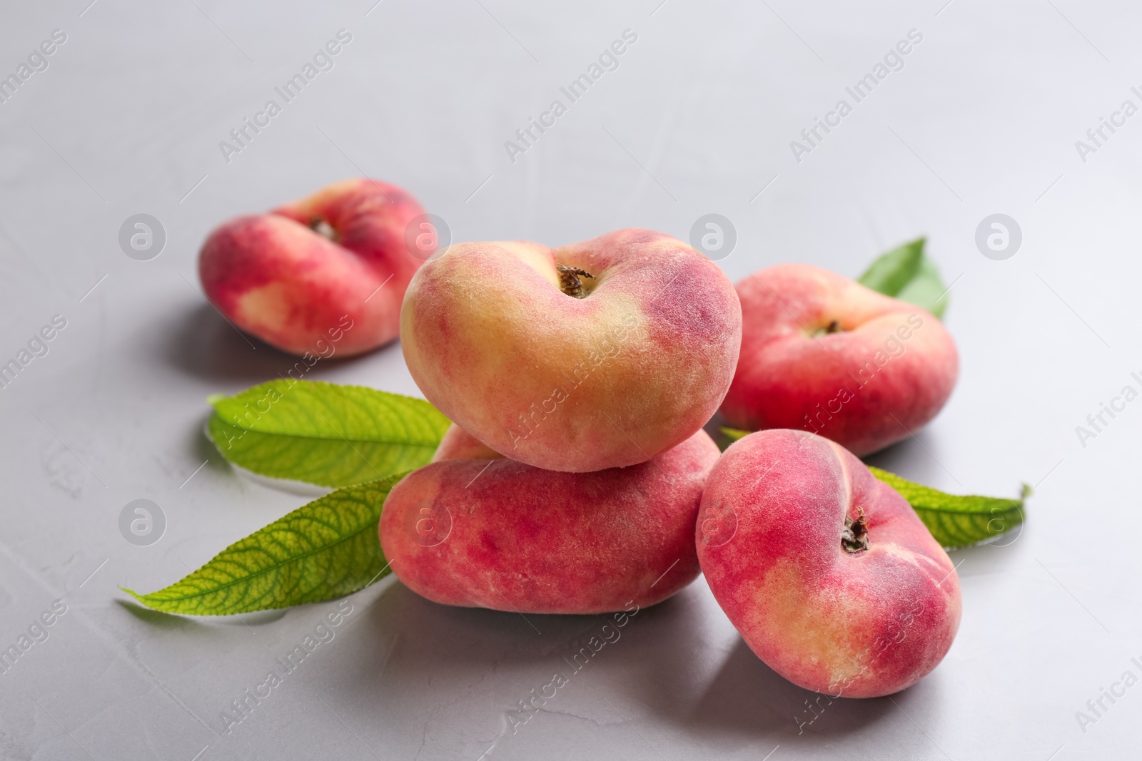 Photo of Fresh ripe donut peaches with leaves on light table, closeup