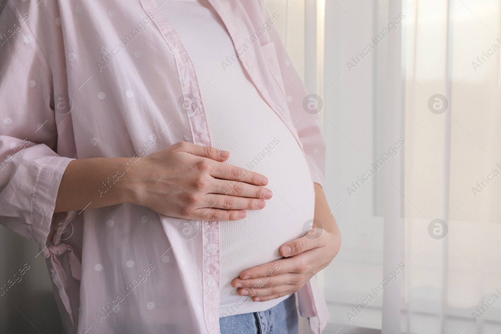 Photo of Young pregnant woman near window at home, closeup. Space for text