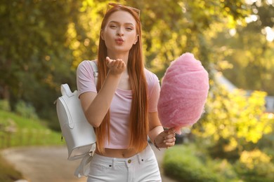 Beautiful woman with cotton candy blowing kiss outdoors on sunny day