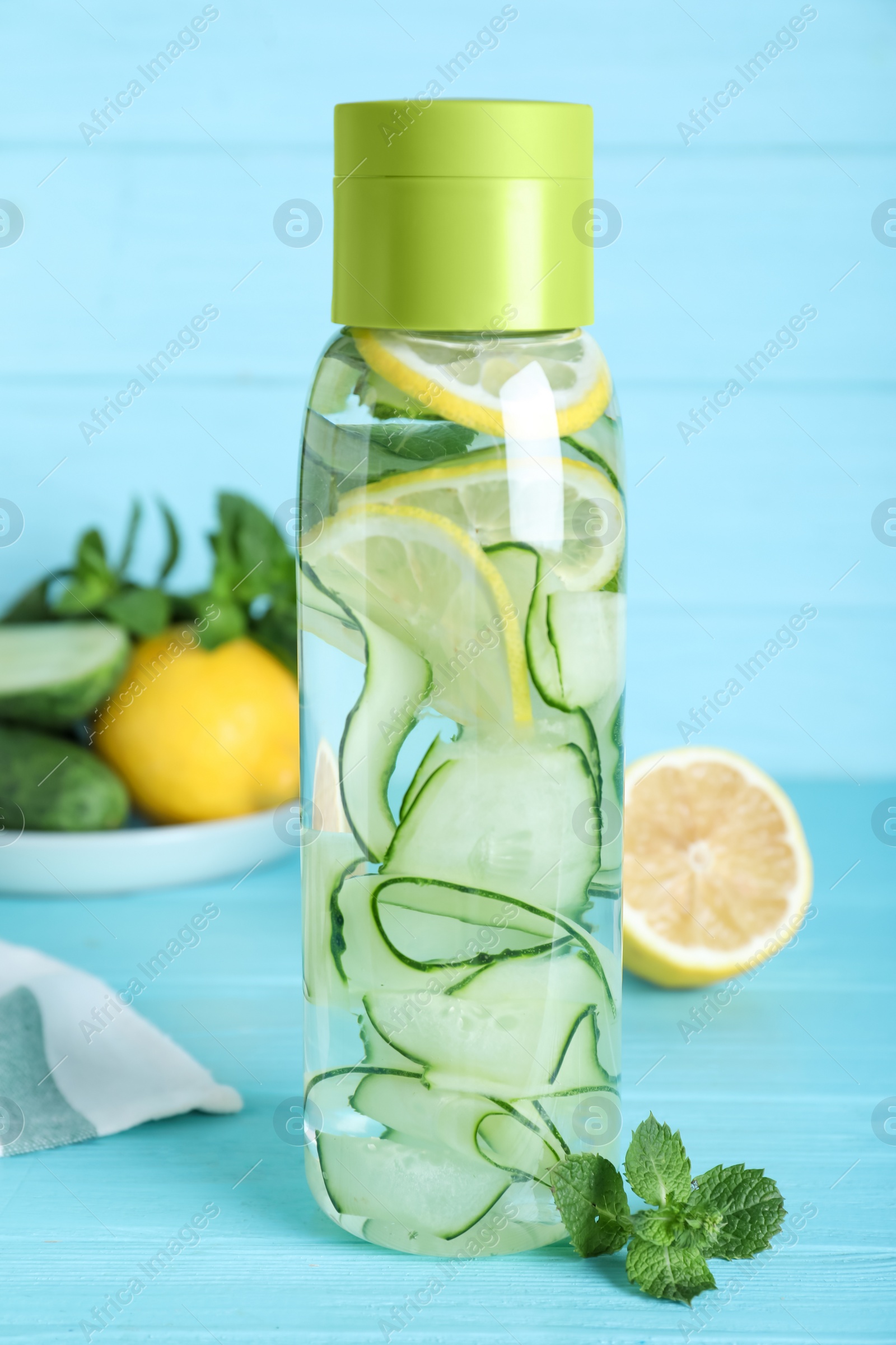 Photo of Bottle of refreshing water with cucumber, lemon and mint on light blue wooden table