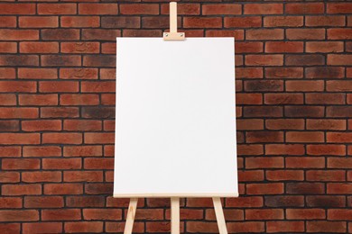 Photo of Wooden easel with blank canvas near brick wall