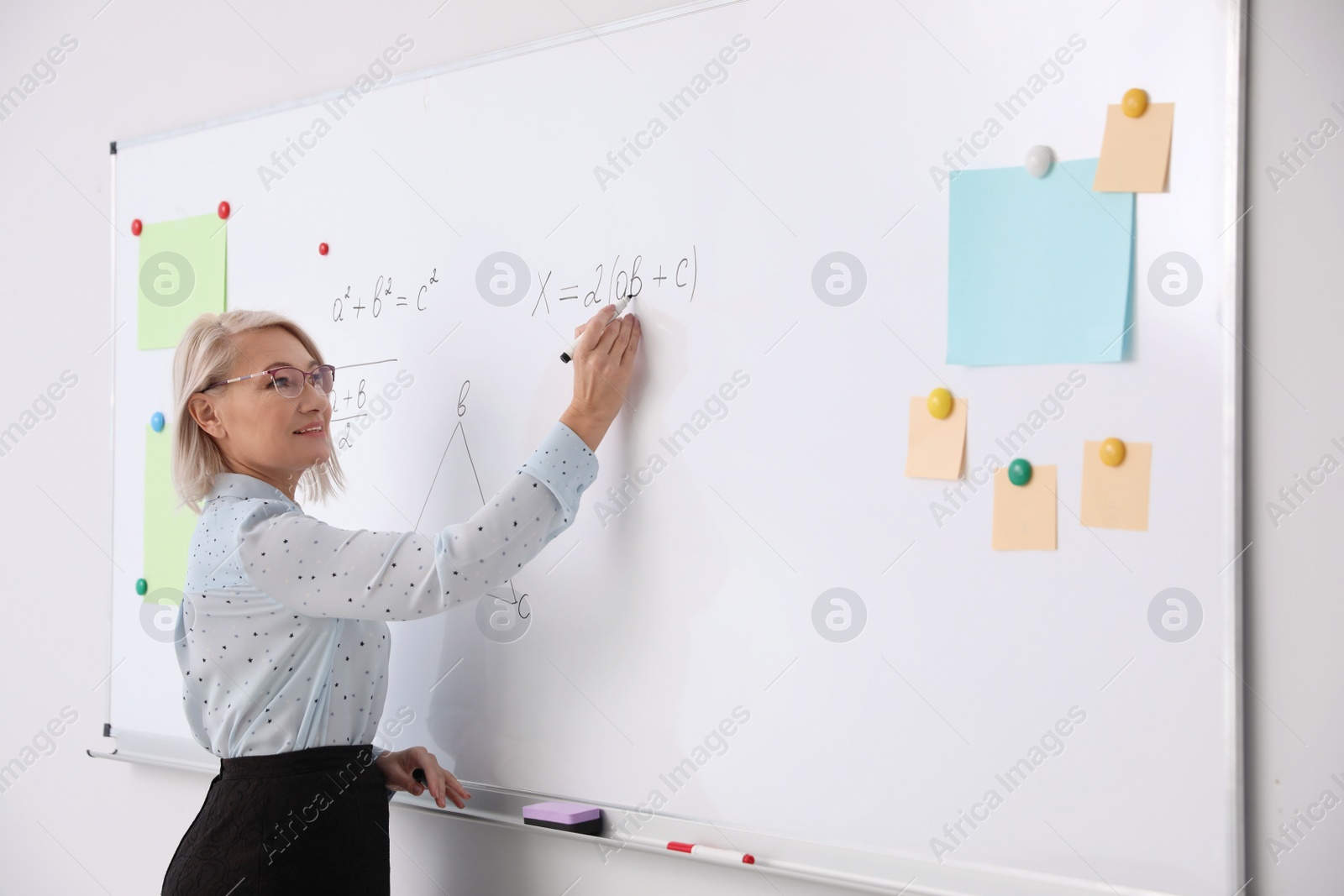 Photo of Mature teacher writing on whiteboard in modern classroom