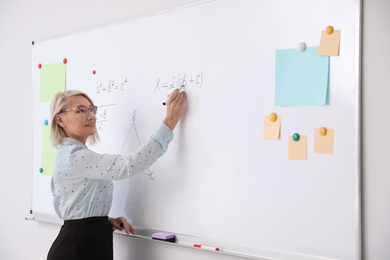 Photo of Mature teacher writing on whiteboard in modern classroom