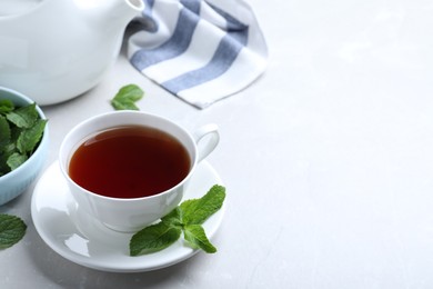 Photo of Cup with hot aromatic mint tea on light table, space for text