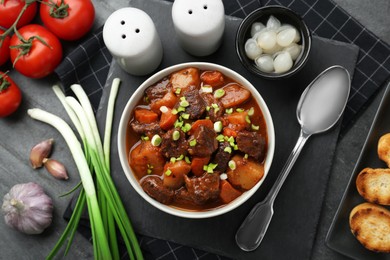 Photo of Delicious beef stew with carrots, green onions and ingredients on grey table, flat lay