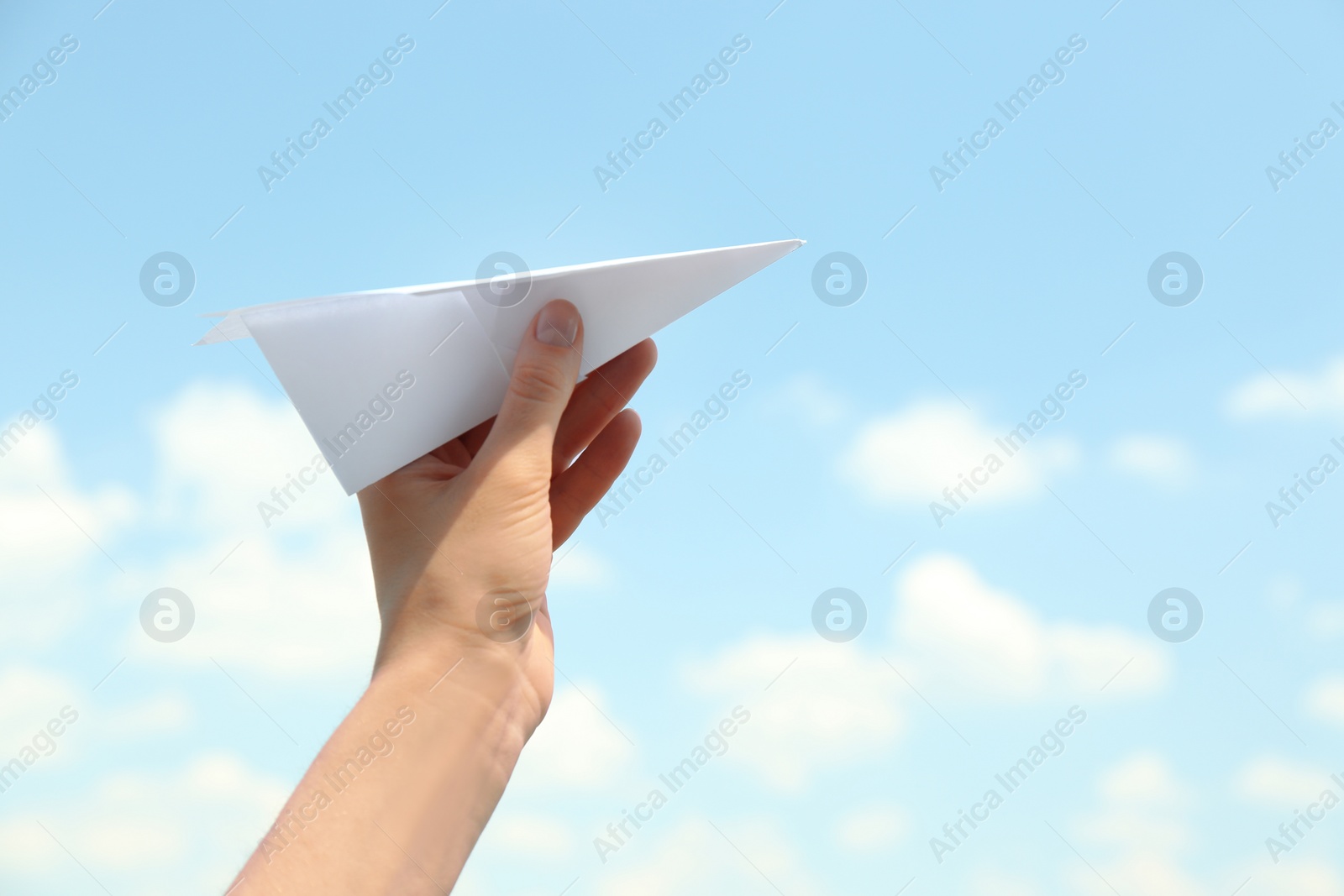 Photo of Woman holding paper plane against blue sky, closeup. Space for text