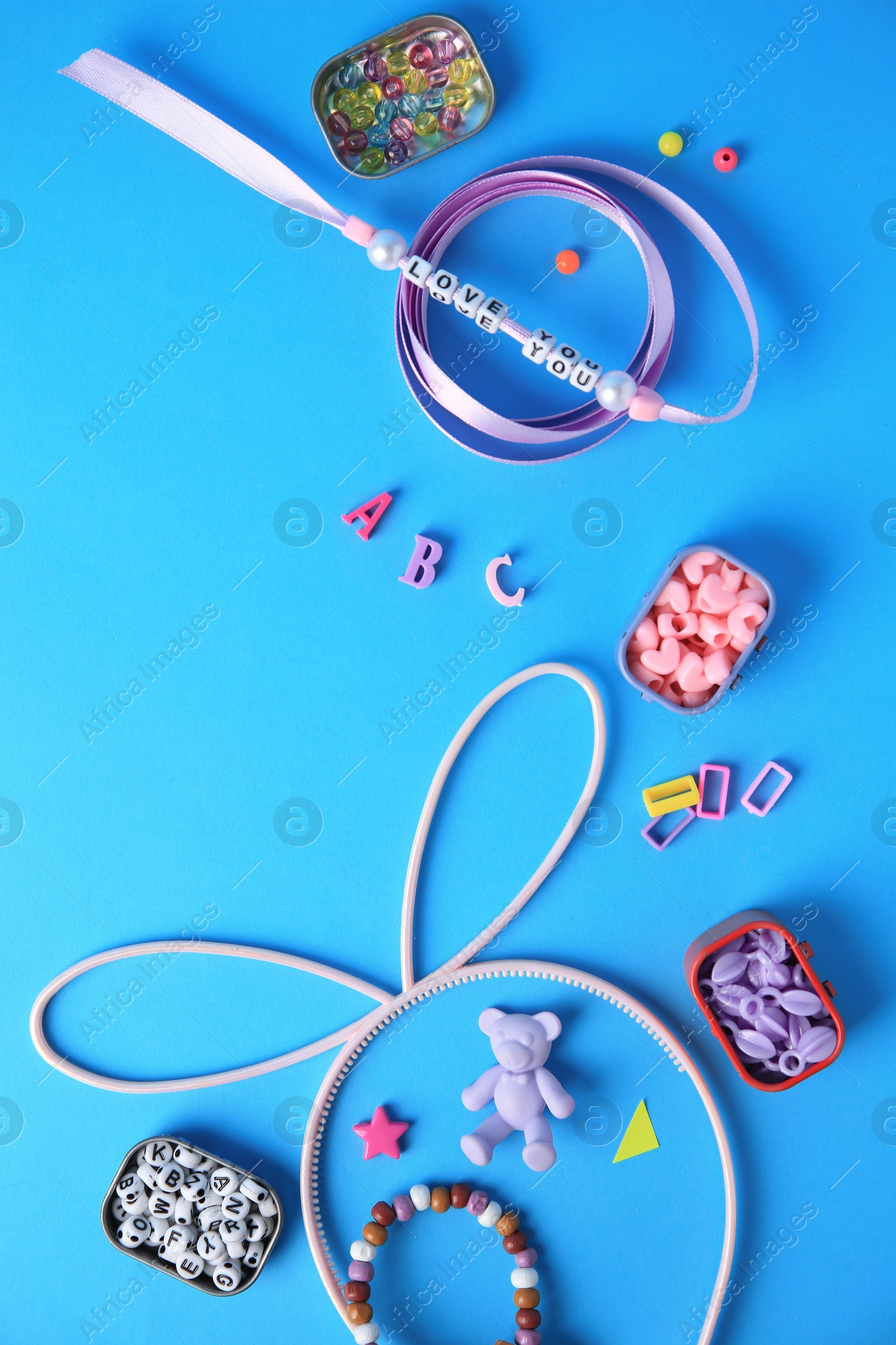 Photo of Handmade jewelry kit for kids. Colorful beads, ribbon and supplies on light blue background, flat lay