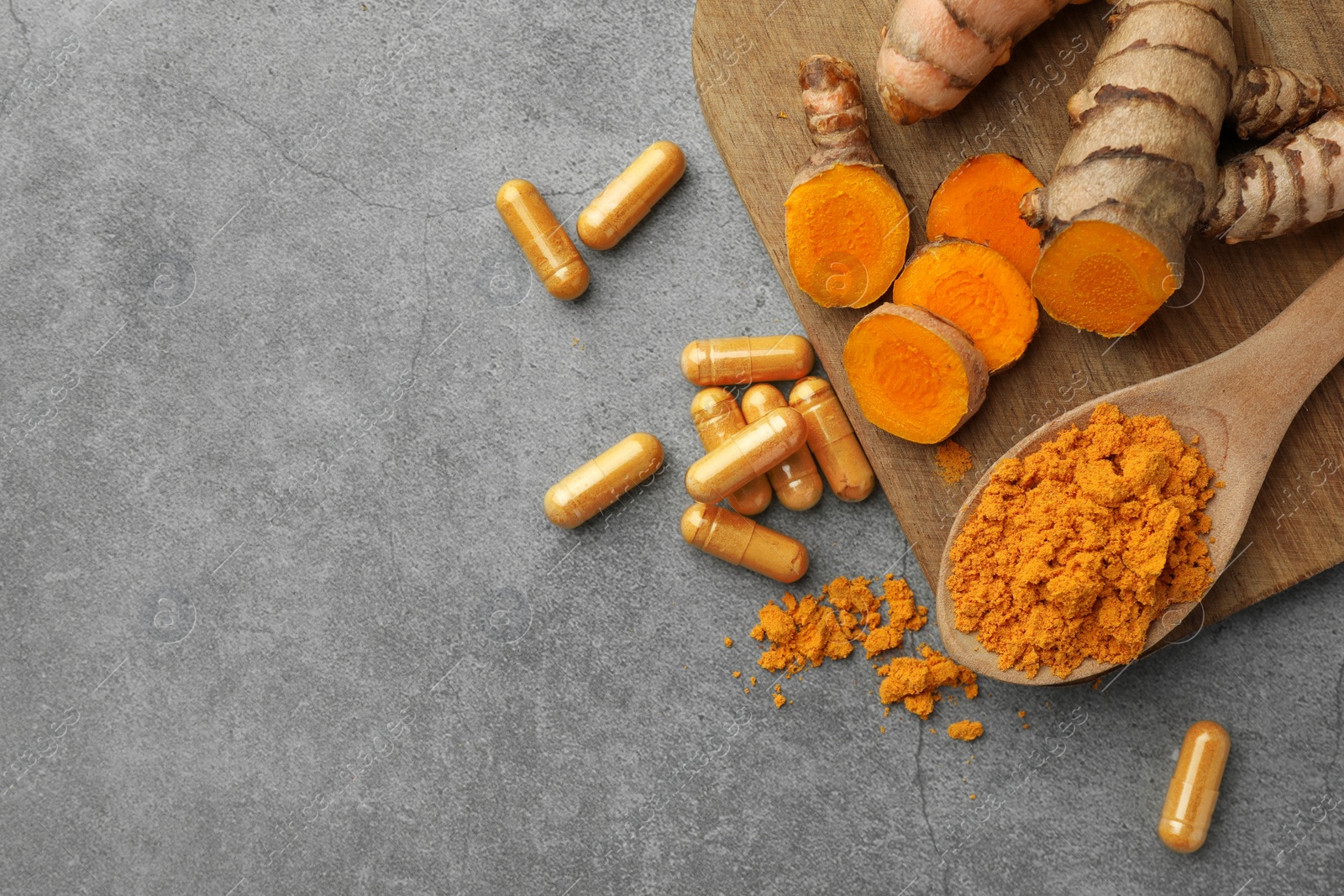 Photo of Aromatic turmeric powder, pills and raw roots on grey table, flat lay. Space for text