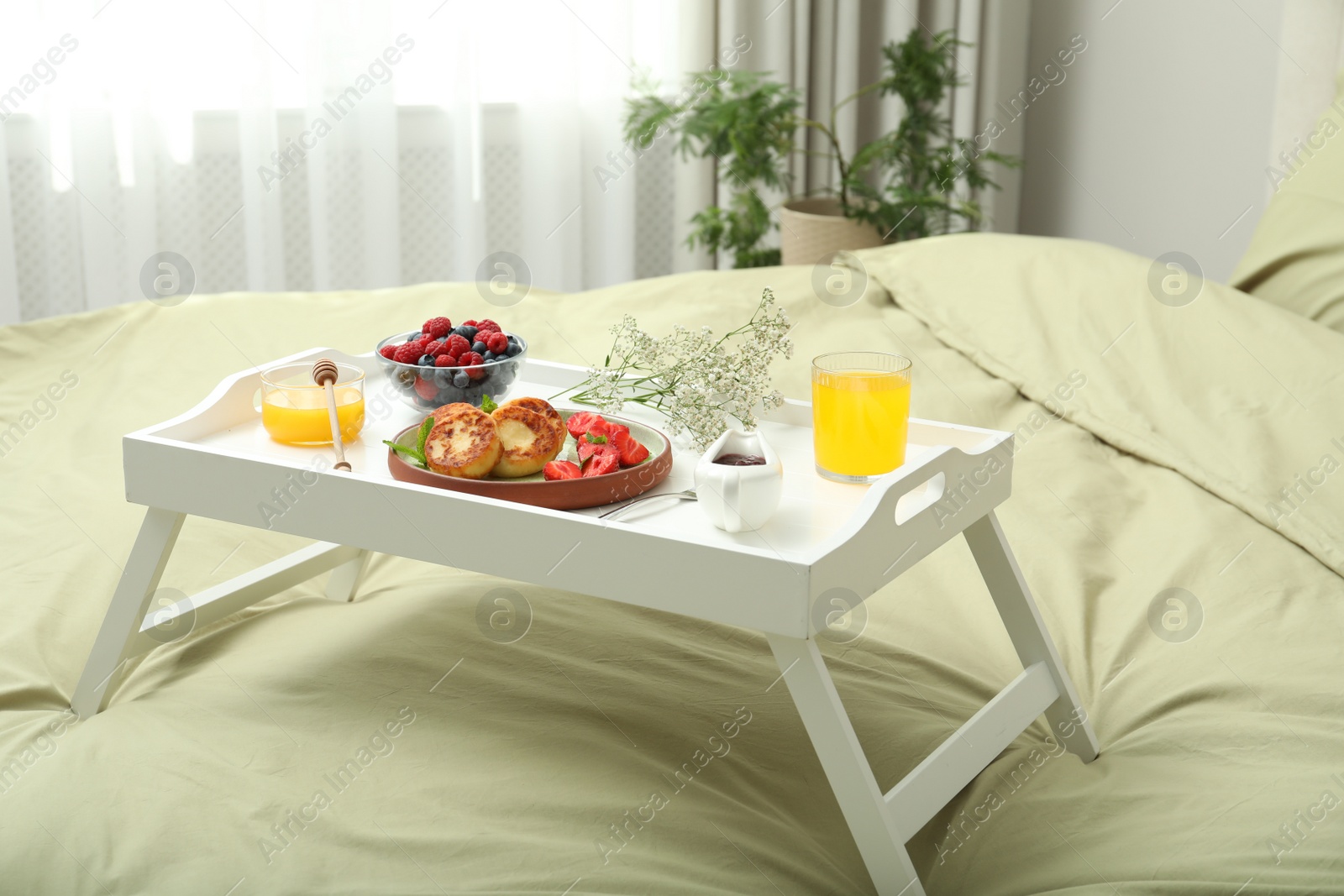 Photo of Tasty breakfast served in bedroom. Cottage cheese pancakes with fresh berries and mint on white tray
