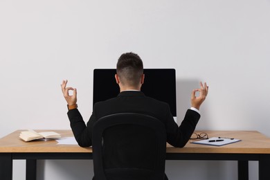 Photo of Businessman meditating at workplace, back view. Zen concept