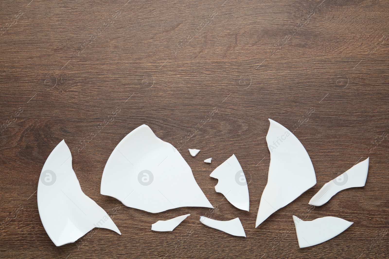 Photo of Pieces of broken ceramic plate on wooden table, flat lay. Space for text