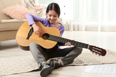 Photo of Cute little girl playing guitar on floor in room