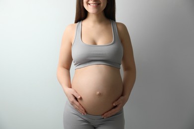 Pregnant young woman touching belly on light background, closeup