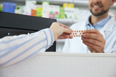 Professional pharmacist giving pills to customer in drugstore, closeup