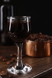 Shot glass with coffee liqueur and beans on wooden table, closeup