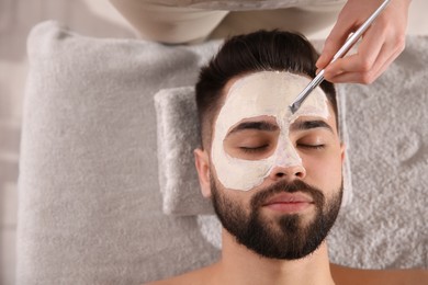 Photo of Cosmetologist applying mask on man's face in spa salon, top view. Space for text