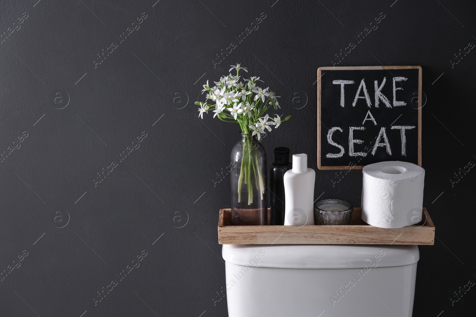 Photo of Decor elements, necessities and toilet bowl near black wall, space for text. Bathroom interior