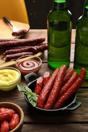 Photo of Thin dry smoked sausages, basil and sauces on wooden table