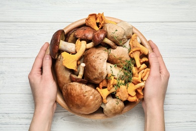 Photo of Woman holding bowl of different wild mushrooms at white wooden table, top view