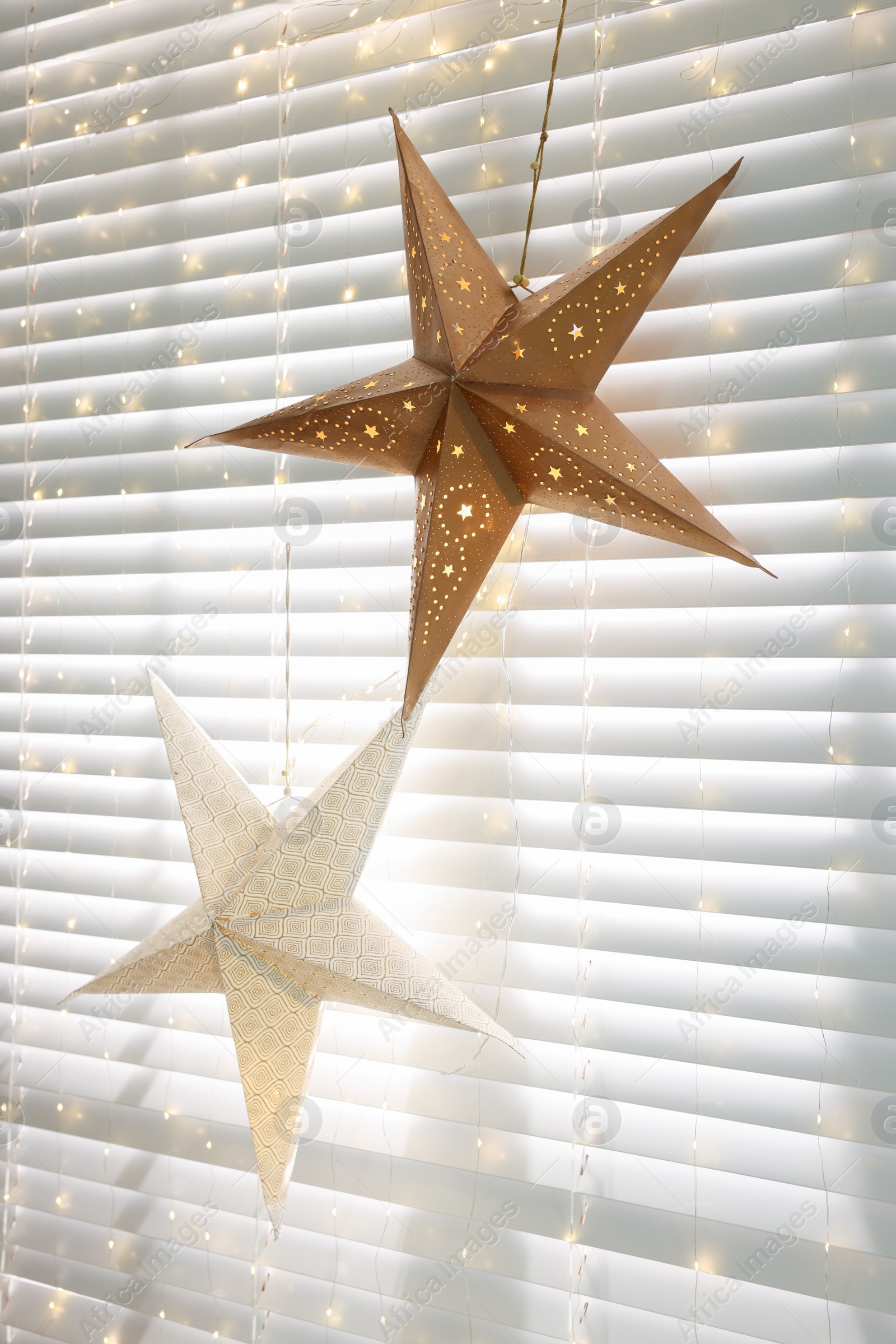 Photo of Beautiful decorative stars and festive lights hanging on window indoors. Christmas atmosphere