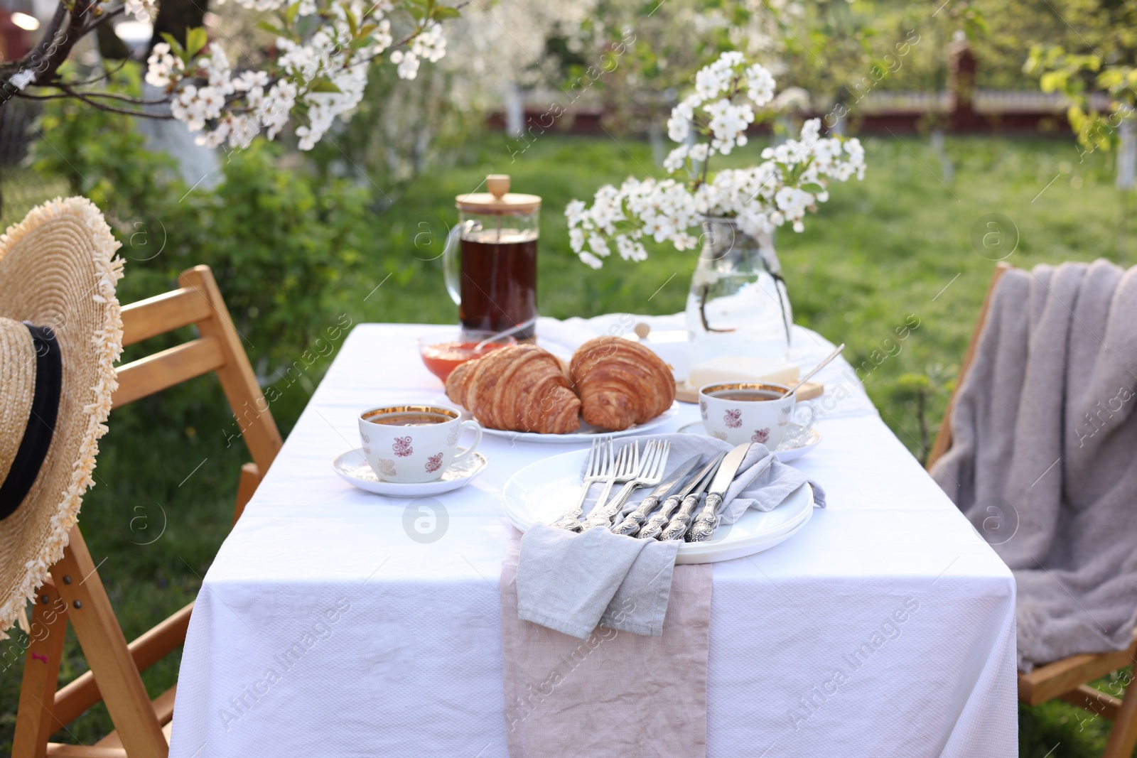 Photo of Stylish table setting with beautiful spring flowers, tea and croissants in garden