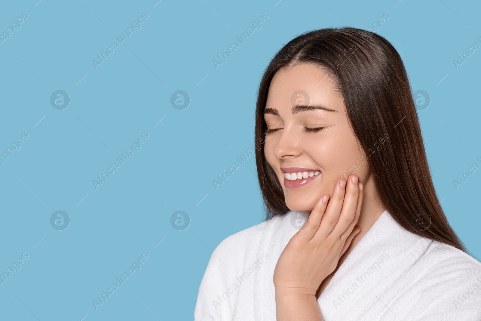 Photo of Portrait of attractive young woman in bathrobe on light blue background, space for text. Spa treatment