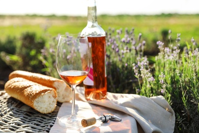 Photo of Composition with glass of wine on wicker table in lavender field