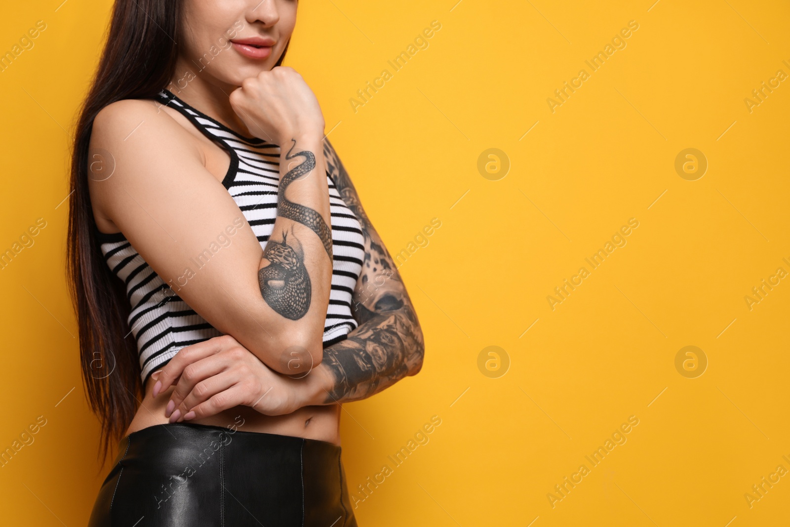 Photo of Beautiful woman with tattoos on arms against yellow background, closeup. Space for text