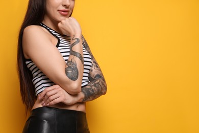 Photo of Beautiful woman with tattoos on arms against yellow background, closeup. Space for text