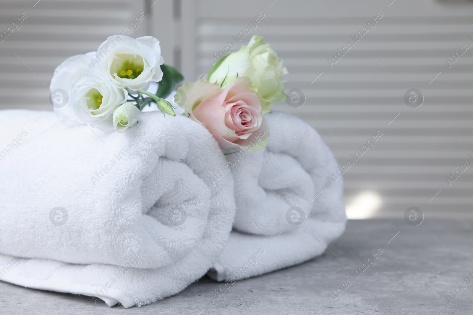 Photo of Rolled towels and flowers on grey table indoors