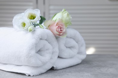 Photo of Rolled towels and flowers on grey table indoors