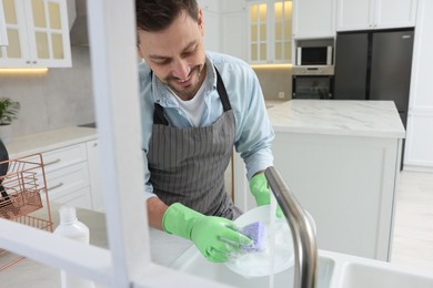 Photo of Man washing plate above sink in kitchen