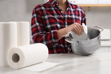 Photo of Woman wiping pan with paper towel at white marble table in kitchen, closeup