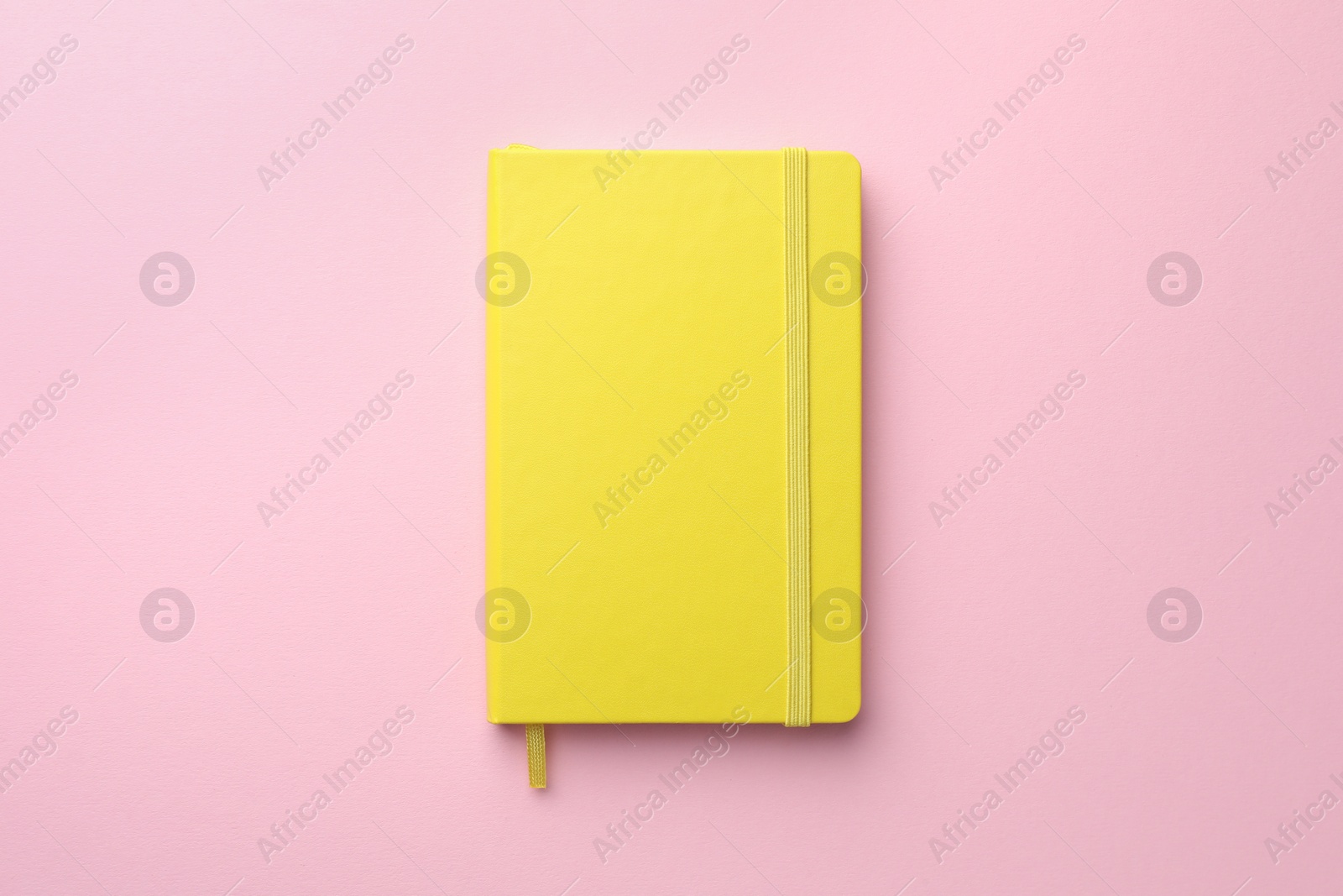 Photo of Closed yellow notebook on light pink background, top view