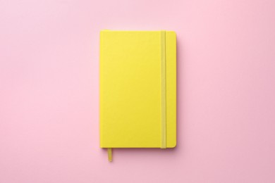 Photo of Closed yellow notebook on light pink background, top view