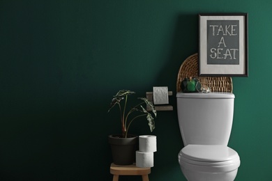 Photo of Decor elements, paper rolls and toilet bowl near green wall, space for text. Bathroom interior